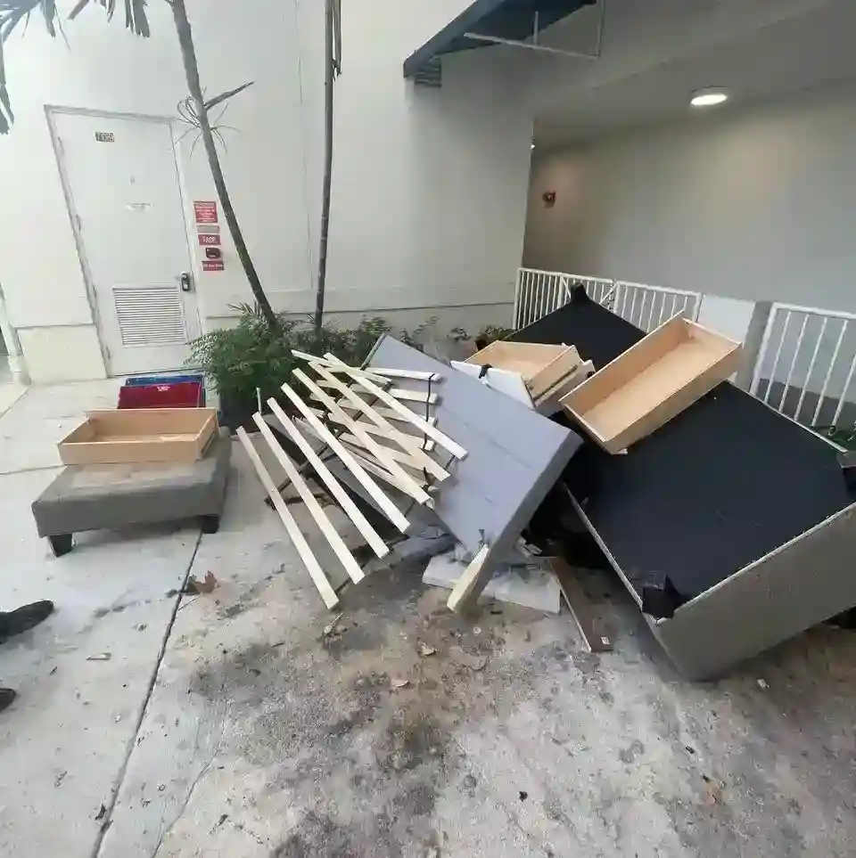 Pile of broken furniture, including a bed frame and drawers, cluttering an apartment patio before junk removal service